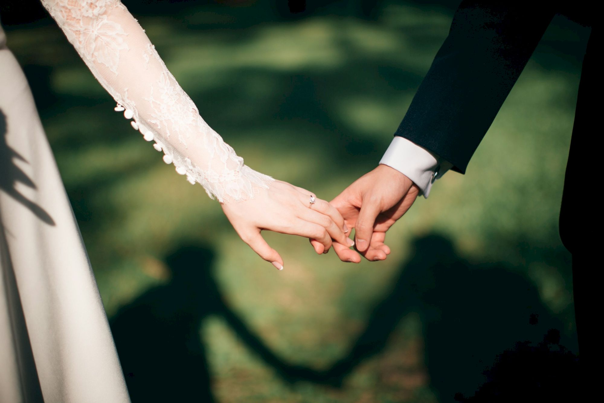 A close-up of a bride and groom holding hands, wedding attire visible, forming a heart-like silhouette in the background.