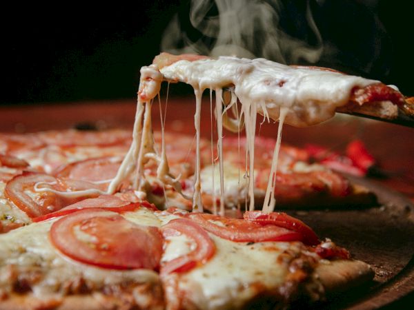 A hot cheese pizza being lifted with melted cheese strings stretching, pepperoni visible, tomato sauce and crust in a close, appetizing shot.
