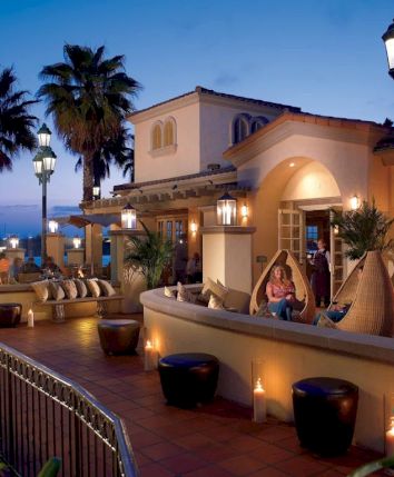 A luxurious seaside resort terrace at dusk, with warm lighting, palm trees, lounge chairs, and couples enjoying the ocean view.